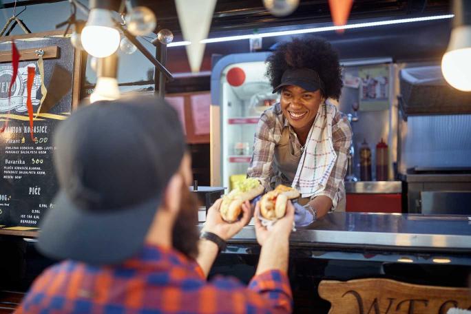 A female food truck employee hands a man his hotdogs - Food Trucks by Guardian Refresh