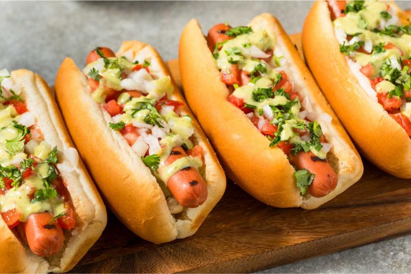 A row of hotdogs on buns topped with condiments.