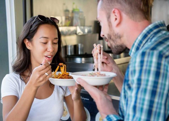 A man and woman enjoying pasta dishes at an outdoor event.