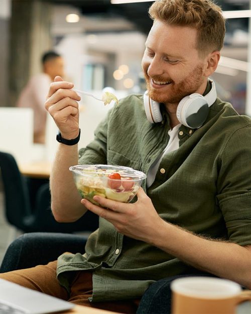 Happy entrepreneur having a healthy meal and eating salad on a break in the office.